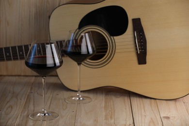 Photo of Acoustic guitar and glasses of red wine on wooden table. Space for text