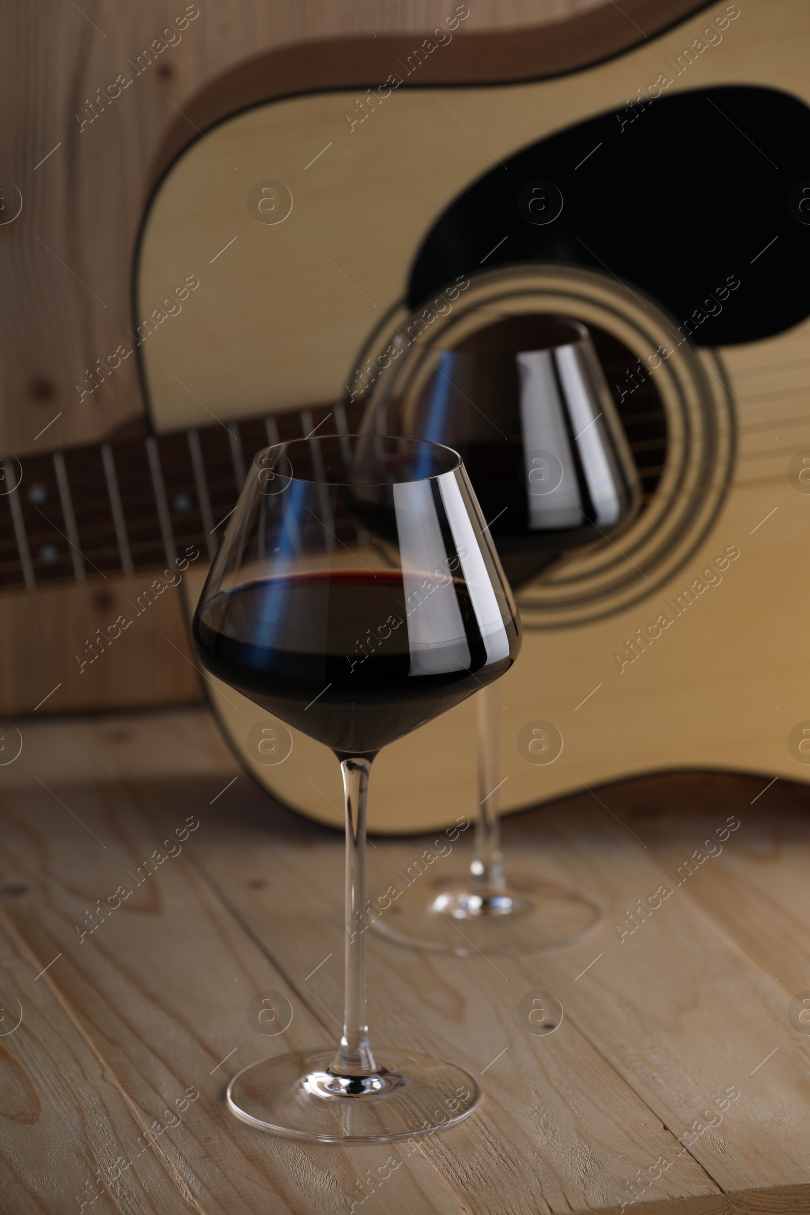 Acoustic guitar and glasses of red wine on wooden table Photo of Acoustic guitar and glasses of red wine on wooden table