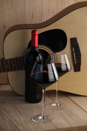 Photo of Acoustic guitar, bottle and glasses of red wine on wooden table