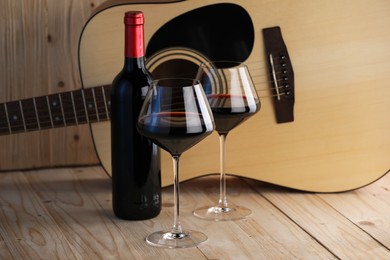 Photo of Acoustic guitar, bottle and glasses of red wine on wooden table