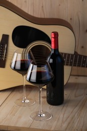 Photo of Acoustic guitar, bottle and glasses of red wine on wooden table