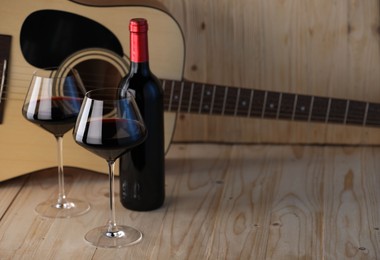 Photo of Acoustic guitar, bottle and glasses of red wine on wooden table. Space for text