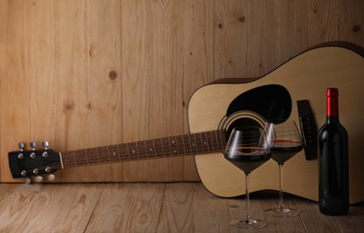 Photo of Acoustic guitar, bottle and glasses of red wine on wooden table. Space for text