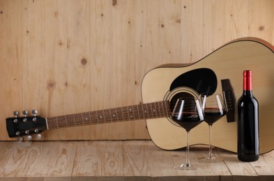 Photo of Acoustic guitar, bottle and glasses of red wine on wooden table. Space for text