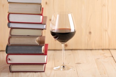 Photo of Glass of red wine and stacked books on wooden table