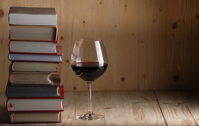Photo of Glass of red wine and stacked books on wooden table. Space for text