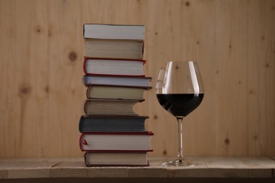 Photo of Glass of red wine and stacked books on wooden table