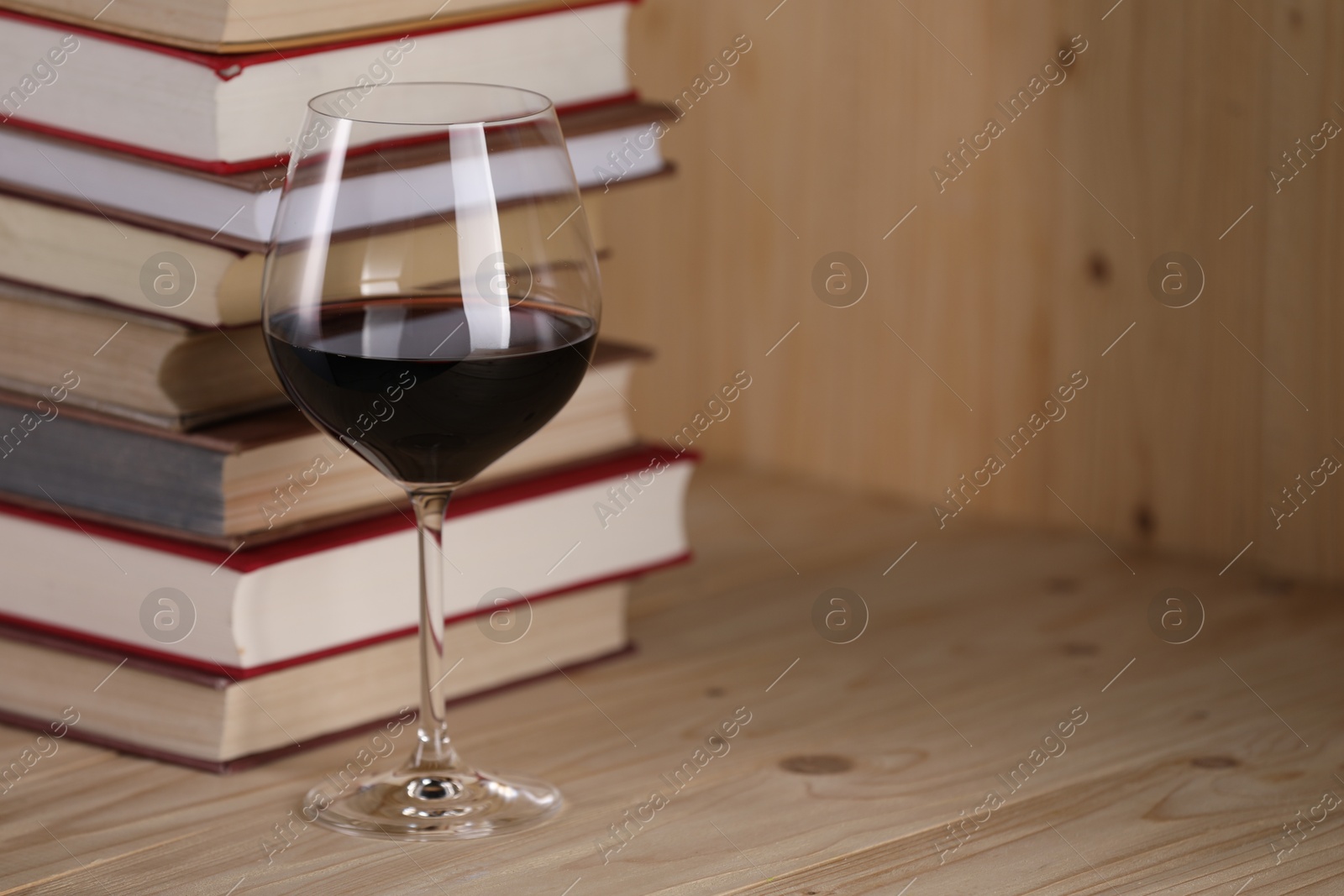 Photo of Glass of red wine and stacked books on wooden table, closeup. Space for text