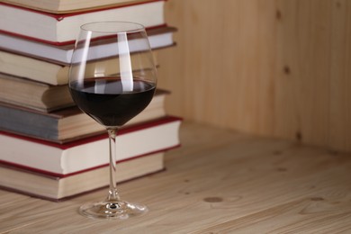 Photo of Glass of red wine and stacked books on wooden table, closeup. Space for text