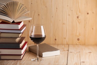 Photo of Glass of red wine and stacked books on wooden table. Space for text