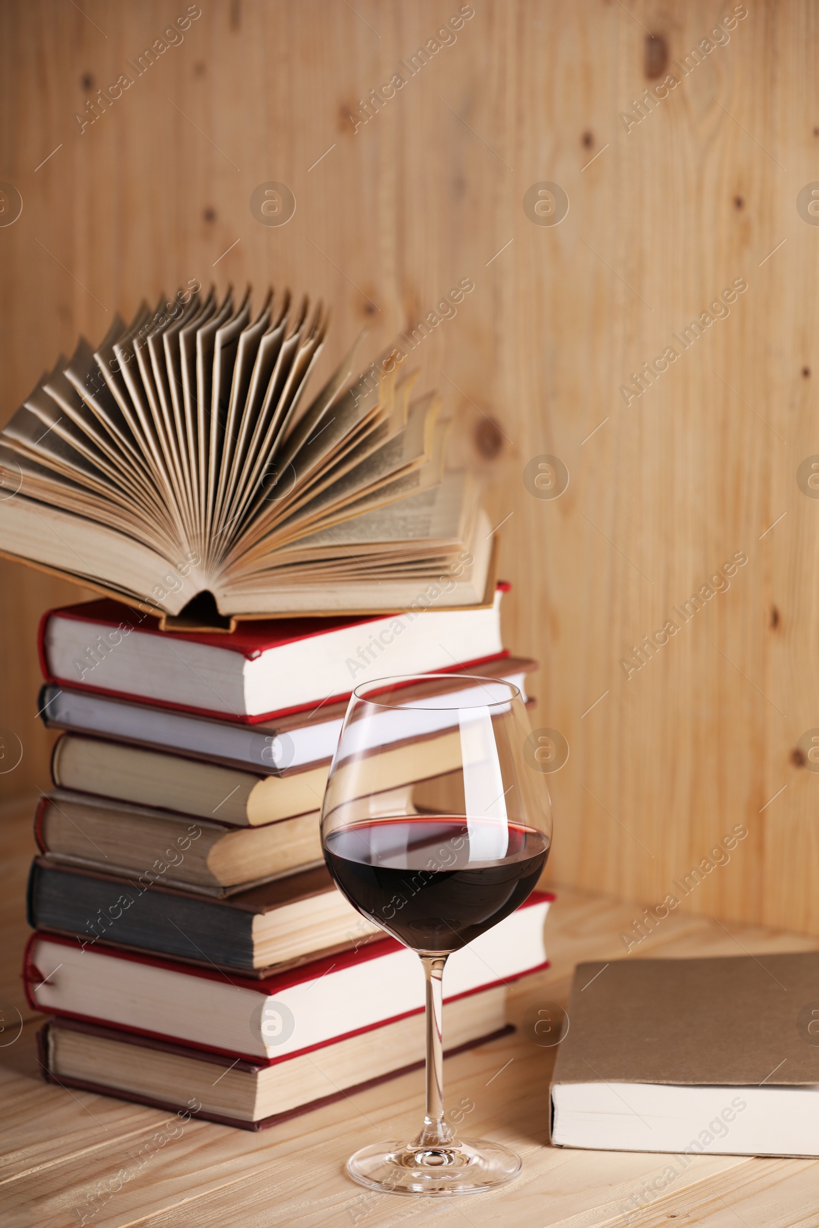 Glass of red wine and stacked books on wooden table Photo of Glass of red wine and stacked books on wooden table