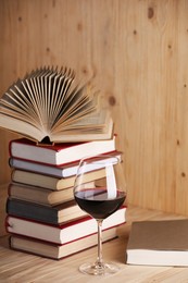 Photo of Glass of red wine and stacked books on wooden table