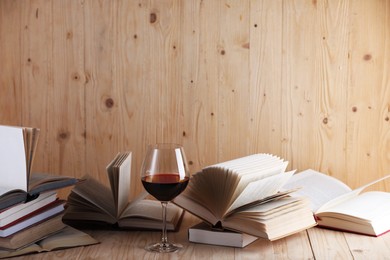 Photo of Glass of red wine and books on wooden table. Space for text
