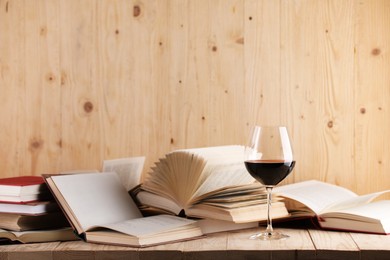 Photo of Glass of red wine and books on wooden table. Space for text