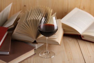 Photo of Glass of red wine and books on wooden table, closeup