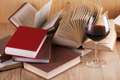 Photo of Glass of red wine and books on wooden table, closeup