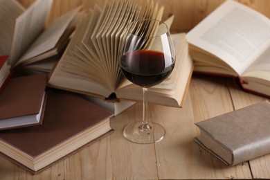 Photo of Glass of red wine and books on wooden table, closeup