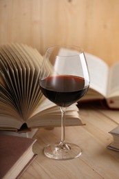 Photo of Glass of red wine and books on wooden table, closeup