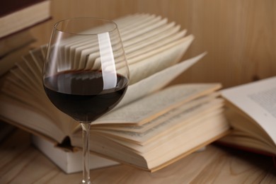 Photo of Glass of red wine and open books on wooden table, closeup
