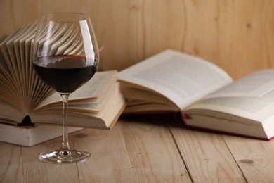 Photo of Glass of red wine and open books on wooden table, closeup. Space for text