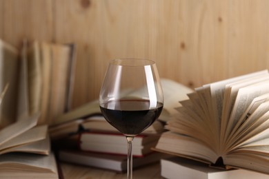 Photo of Glass of red wine and open books on table, closeup