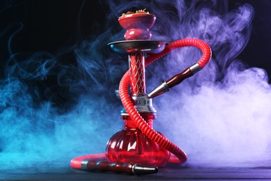 Photo of Hookah on wooden table with smoke in color lights against black background