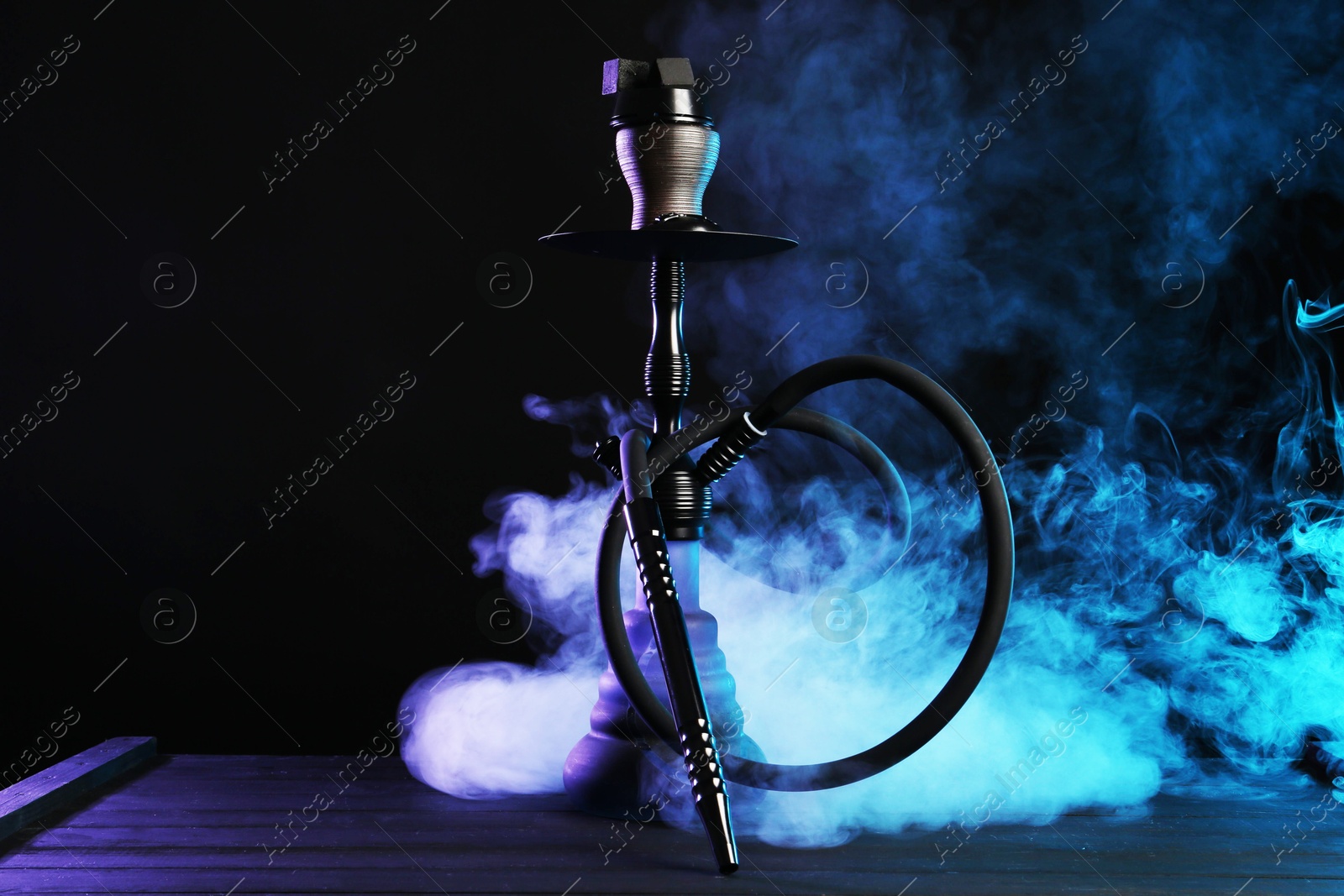 Hookah on wooden table with smoke in color lights against black background Photo of Hookah on wooden table with smoke in color lights against black background