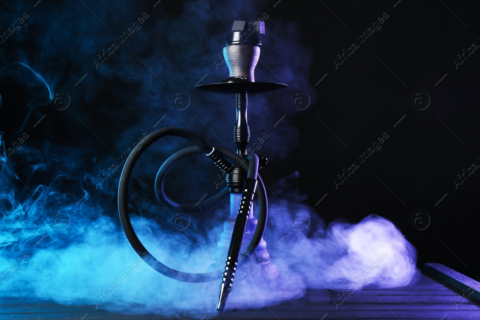 Hookah on wooden table with smoke in color lights against black background Photo of Hookah on wooden table with smoke in color lights against black background