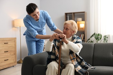 Photo of Nurse assisting senior woman with walking cane indoors. Home health care service