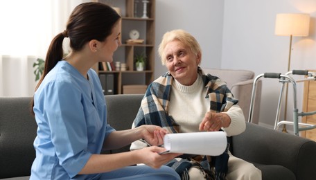 Photo of Nurse with clipboard examining senior woman indoors. Home health care service