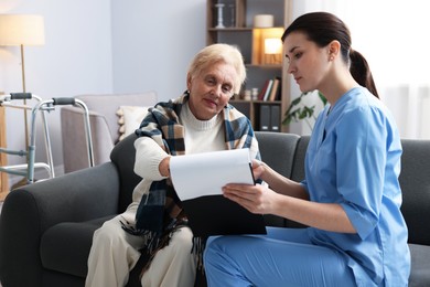 Photo of Nurse with clipboard examining senior woman indoors. Home health care service