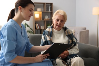Photo of Nurse with clipboard examining senior woman indoors. Home health care service