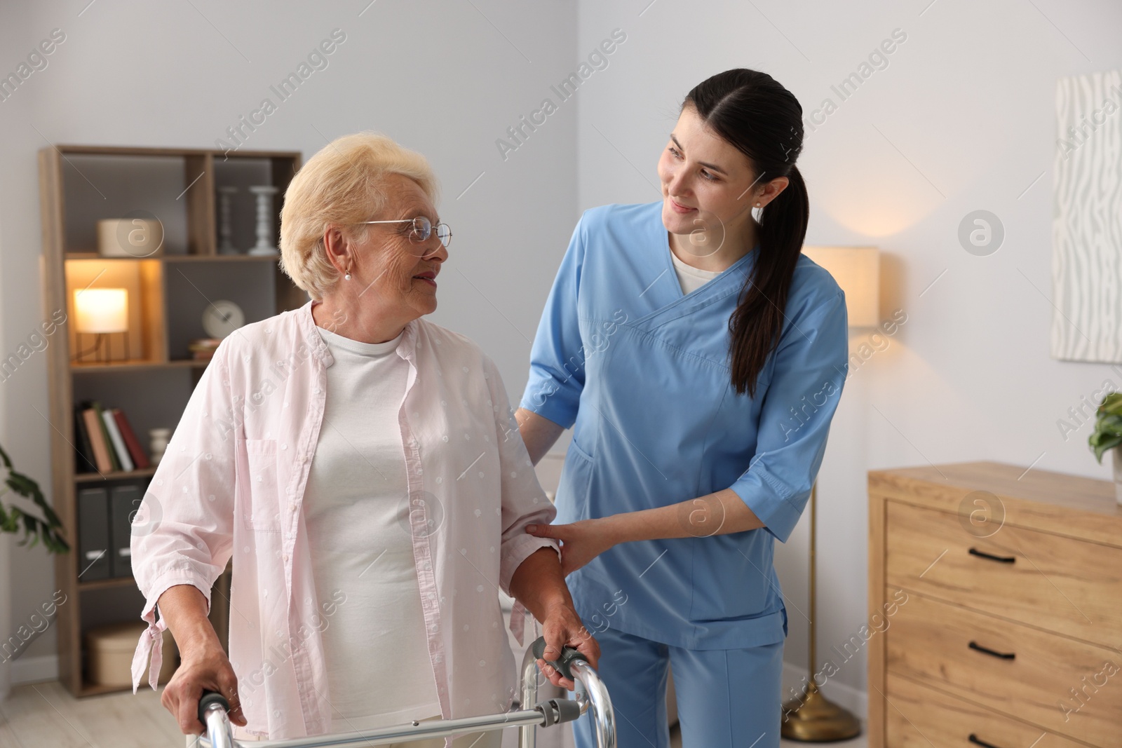 Nurse assisting senior woman with walking frame indoors. Home health care service Photo of Nurse assisting senior woman with walking frame indoors. Home health care service