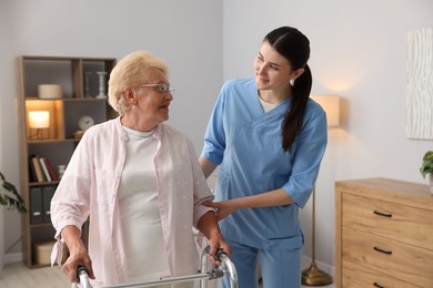 Photo of Nurse assisting senior woman with walking frame indoors. Home health care service