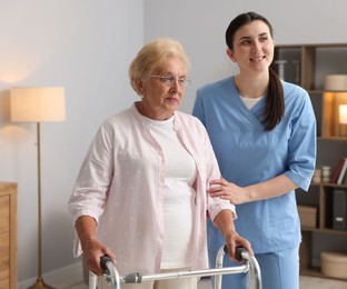 Photo of Nurse assisting senior woman with walking frame indoors. Home health care service