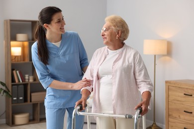 Photo of Nurse assisting senior woman with walking frame indoors. Home health care service