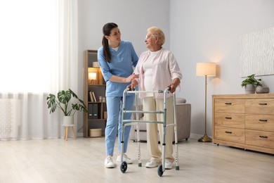 Photo of Nurse assisting senior woman with walking frame indoors. Home health care service