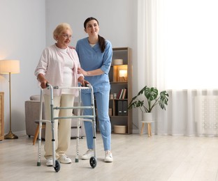 Photo of Nurse assisting senior woman with walking frame indoors, space for text. Home health care service