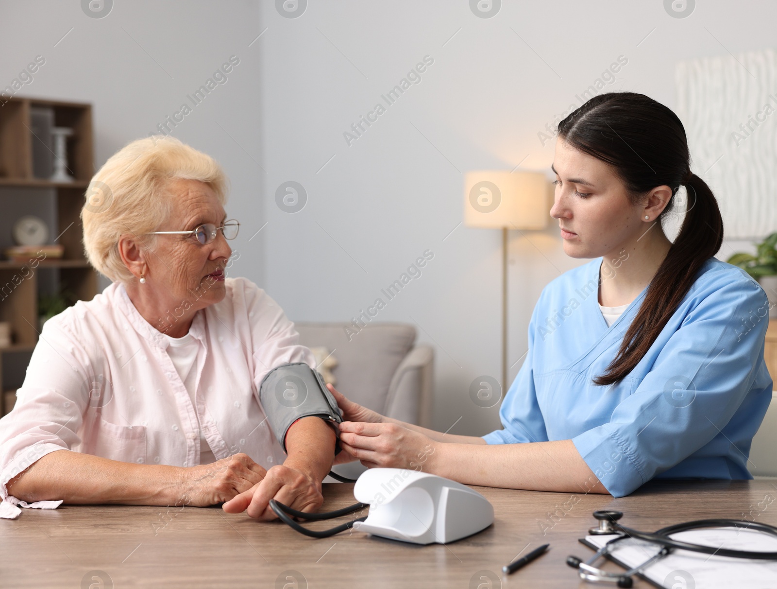 Photo of Nurse measuring patient's blood pressure at wooden table indoors. Home health care service