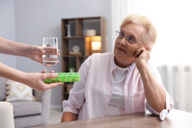 Photo of Nurse giving glass of water and pills to senior woman indoors, closeup. Home health care service
