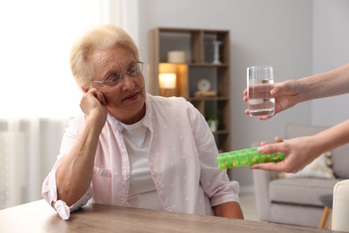 Photo of Nurse giving glass of water and pills to senior woman indoors, closeup. Home health care service