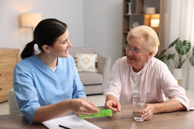 Photo of Nurse giving pills to senior woman at wooden table indoors. Home health care service