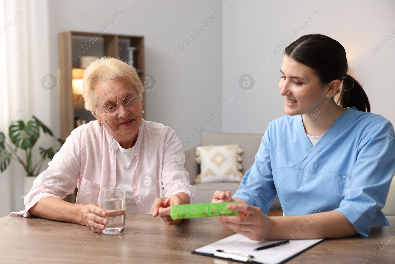 Photo of Nurse giving pills to senior woman at wooden table indoors. Home health care service