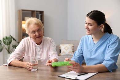 Photo of Nurse giving pills to senior woman at wooden table indoors. Home health care service