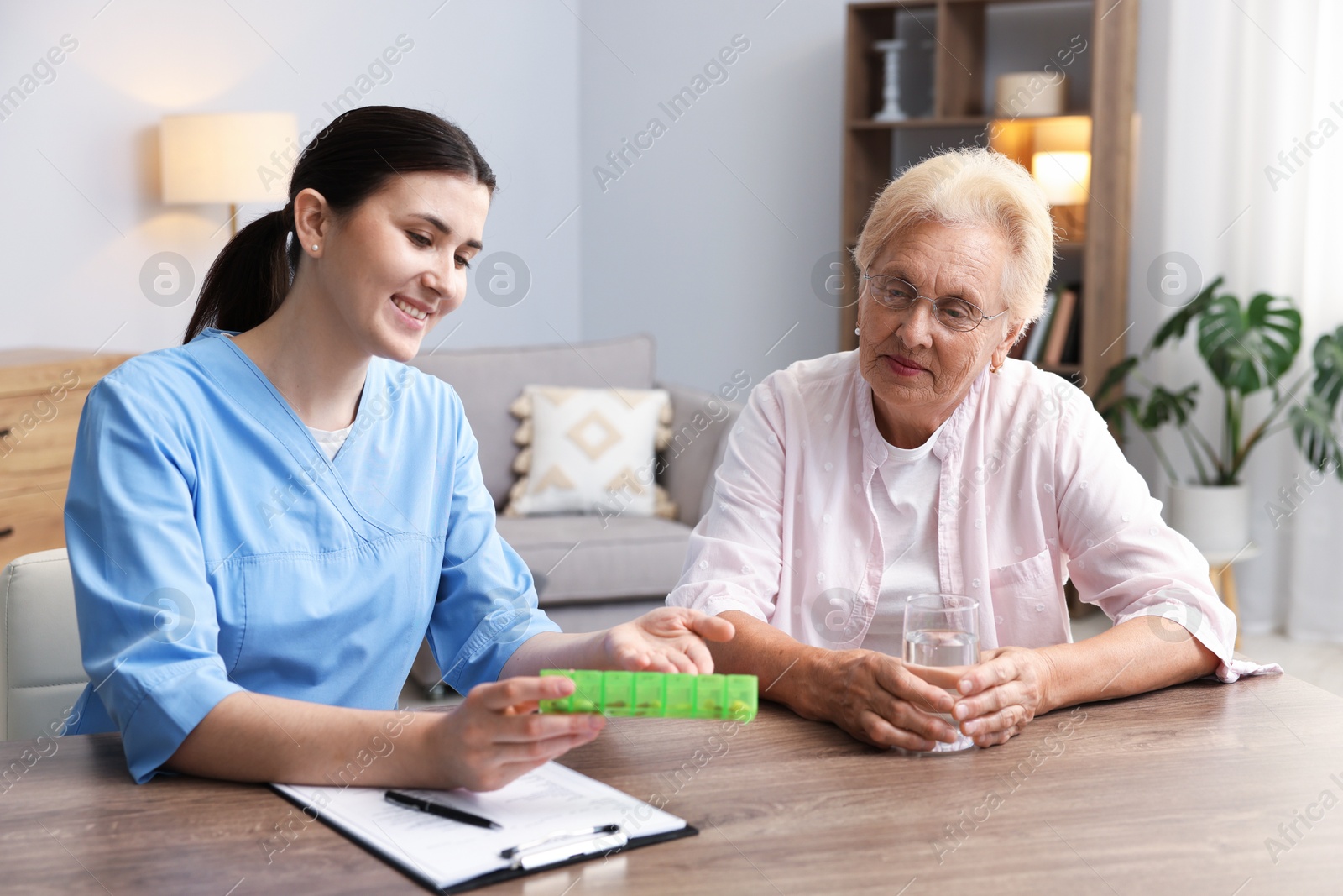 Photo of Nurse giving pills to senior woman at wooden table indoors. Home health care service