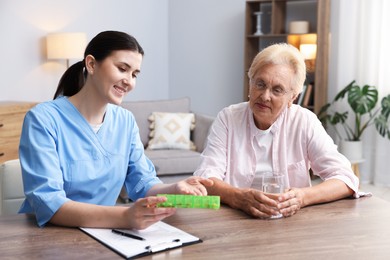 Photo of Nurse giving pills to senior woman at wooden table indoors. Home health care service