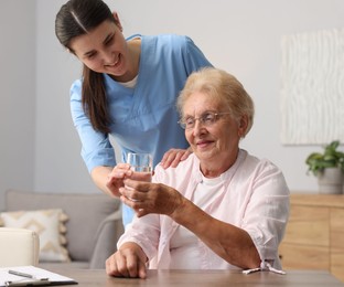 Photo of Nurse giving glass of water to senior woman indoors. Home health care service