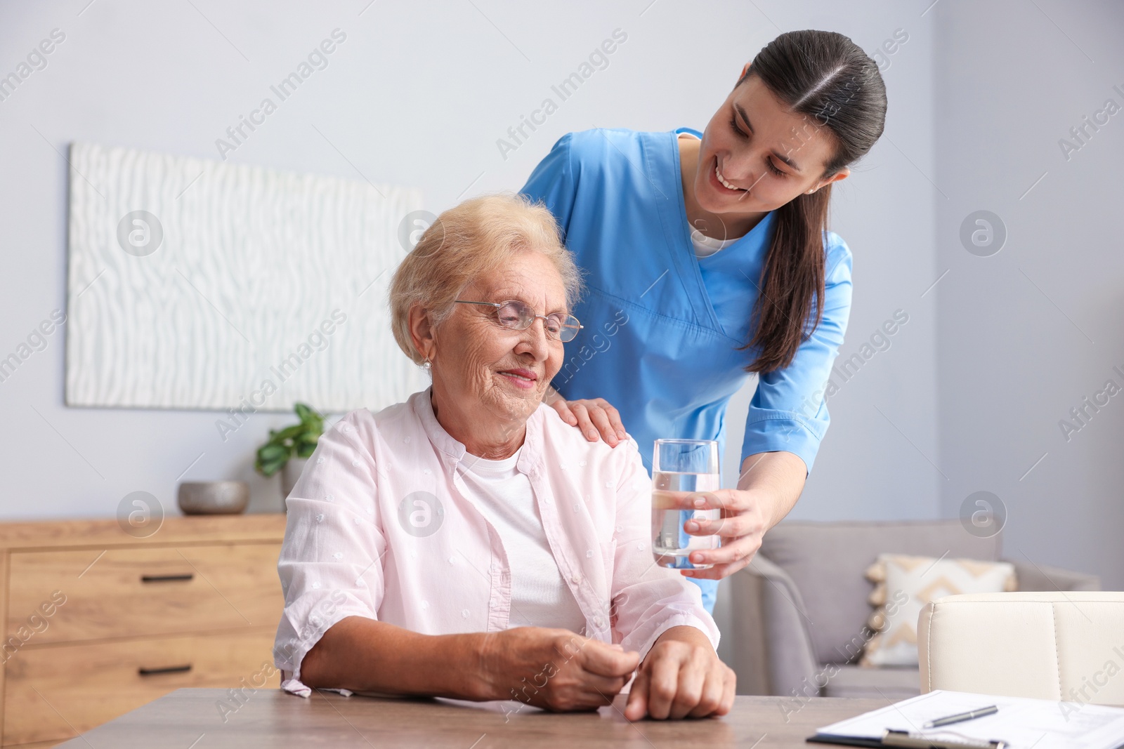 Photo of Nurse giving glass of water to senior woman indoors. Home health care service
