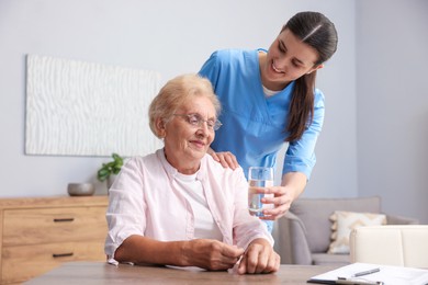 Photo of Nurse giving glass of water to senior woman indoors. Home health care service