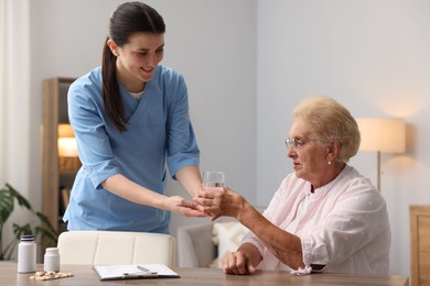 Photo of Nurse giving glass of water to senior woman indoors. Home health care service